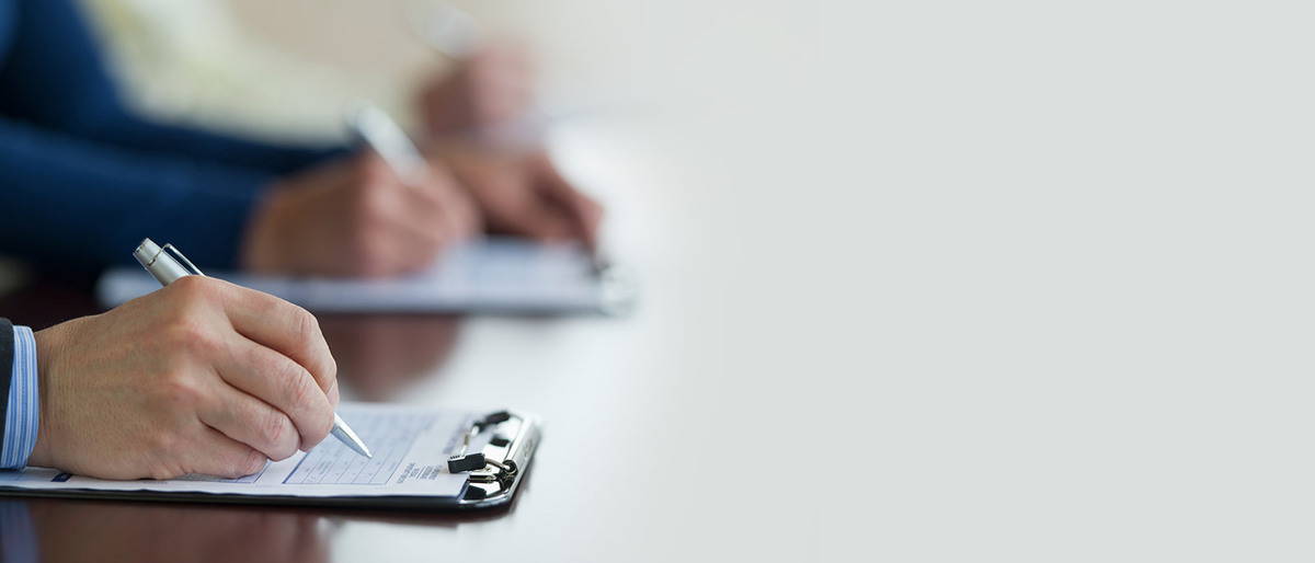 Two people writing on clipboards, one persons hands blurred in background